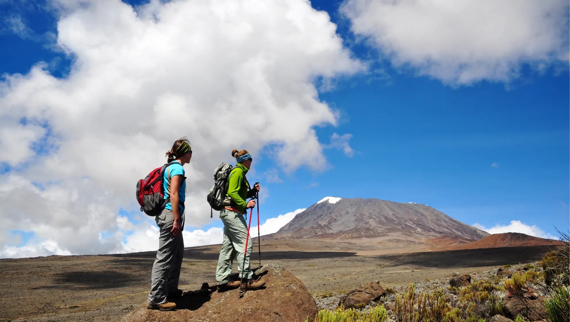 Two trekkers on open moorland looking toward Kilimanjaro's summit cone