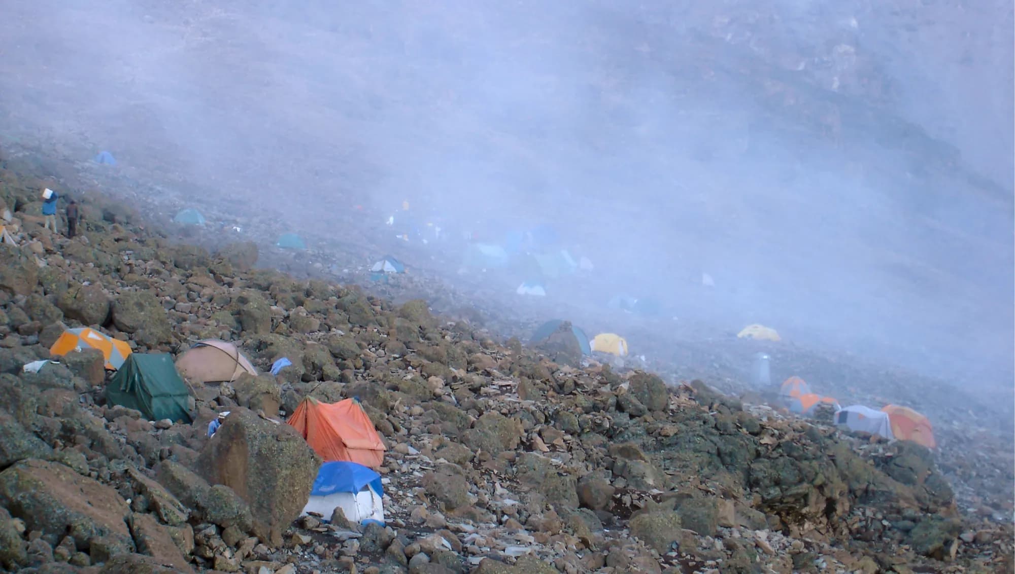 Tents on a rocky slope in drifting cloud at a high Kilimanjaro camp